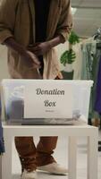 Vertical video Customers donating stylish formal clothes in thrift shop, doing good deed. Generous clients adding their garments in donation box for charitable event organized by SH clothing store