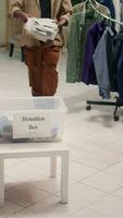 vertical vídeo africano americano clientela en Moda boutique donando su ropa para bueno causa. clientes colocación vestidos en donación caja, haciendo filantropía gesto en ropa Tienda video