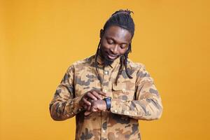 Portrait of businessman looking at wristwatch checking time, being late at work. African american entrepreneur worrying and being impatient about punctuality in studio over yellow background. photo