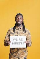 Company entrepreneur holding hiring application sign at camera, advertising corporate job offer and business career opportunity. African american man preparing interview for recruiting applicant. photo