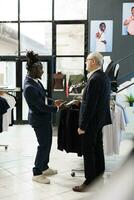 africano americano trabajador Ayudar cliente con formal traje en ropa almacenar, cliente mirando a comprar moderno ropa. mayor cliente comprando de moda mercancías y de moda accesorios en sala de exposición foto