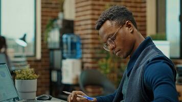 Corporate assistant taking notes on files, reviewing business documents and statistics to create new research plan. Young man in coworking space examining annual reports with information. photo