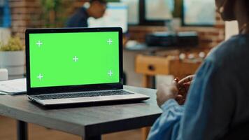 Woman checking green screen display in startup office, looking at isolated chroma key template. Female employee using blank copyspace and mockup on laptop, business coworking space. photo