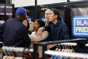 Crowd of diverse people standing at clothing store entrance going crazy during Black Friday. Shoppers arguing fighting with African American man security guard while waiting in line. Bargain hunting photo