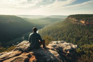 Man sitting on the edge of cliff and looking at the valley, Man sitting on cliff edge alone enjoying aerial view backpacking lifestyle travel adventure outdoor, AI Generated photo