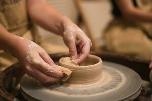 Potter girl works on potter's wheel, making ceramic pot out of clay in pottery workshop photo