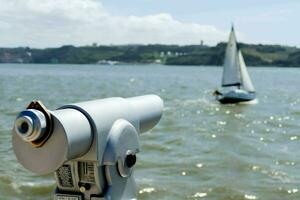 a telescope is looking out over the water with a sailboat in the background photo