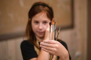 A girl in a creative workshop holds brushes for coloring a clay product photo