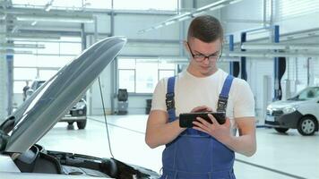 joven mecánico mecanografía en su tableta a el coche Servicio video