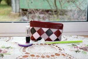 Cosmetic bag, powder, lipstick with an artificial calla flower on a table with a knitted napkin near the window, horizontal photo