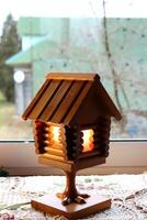 A wooden retro lamp in the form of a hut on chicken legs, a fairy-tale house with glowing windows against the window in the village. Vertical photo, background with space for text photo