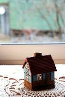 Ceramic candlestick in the shape of a house with a burning candle inside against a window in the village. Model of a house with burning windows, vertical photo, background with space for text photo