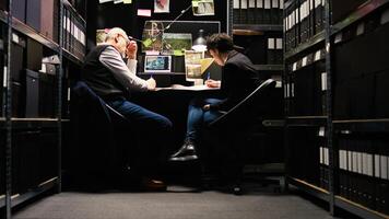 Partners write information about suspect, taking notes on case files before receiving landline phone call. Detectives team uncovering details about forensic evidence, confidential files. photo