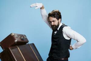 Cheerful porter having fun in studio and showing confidence with crazy funny dance moves against blue background. Hotel concierge employee dancing around and being silly in studio. photo