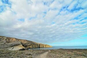 a path leads to the ocean and a cloudy sky photo