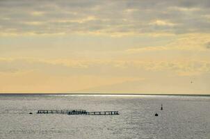 a boat in the ocean with a dock and a sky photo