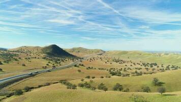 Traffic on Highway and Hilly Rural Green Landscape on Sunny Day. Kern County. California, USA. Aerial View. Drone Flies Backwards video