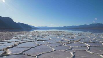Badwater Basin at Sunny Day. Salt Crust Formations with Water and Blue Sky. Death Valley National Park. California, USA. Panning video