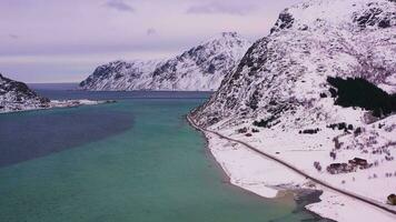 Straße, Fahnenpollen und Berge im Winter. wolkig Himmel. Flakstadoya, Lofoten Inseln, Norwegen. Antenne Sicht. Drohne fliegt seitwärts, Neigung oben video