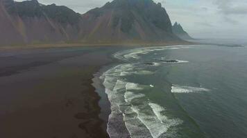 Vestrahorn Berg und Meer Küste. schwarz Sand Strand und Wellen. stokksnes Halbinsel. Island. Antenne Sicht. Drohne fliegt nach vorne, Neigung oben video