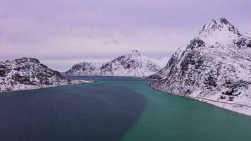 camino, polen de bandera y montañas en invierno. nublado cielo. flakstadoya, lofoten islas, Noruega. aéreo vista. zumbido moscas adelante y hacia arriba video