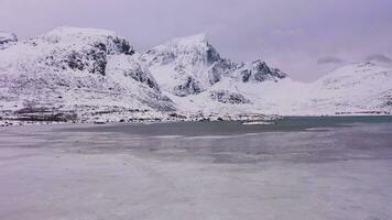 congelé Lac pollen de drapeau et montagnes dans l'hiver. nuageux ciel. flakstadoya, lofoten îles, Norvège. aérien voir. drone mouches vers l'avant et vers le haut video