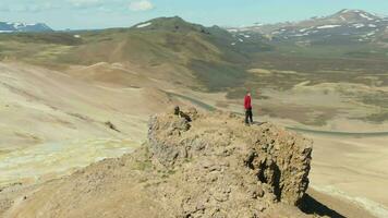 hombre soportes en montaña parte superior mirando en islandés paisaje en soleado día. Islandia. aéreo vista. zumbido es orbital video