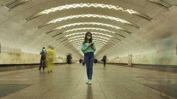 Moskou, Rusland - mei 25, 2020 tijd vervallen van vrouw in masker staand nog steeds in ondergronds metro station en gebruik makend van smartphone gedurende coronavirus covid-19 pandemie. menigte van mensen en voorbijgaan treinen. video