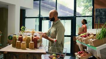 eco consciente persona comprando Fresco comida en local tienda de comestibles Tienda con de cosecha propia mercancías, mirando para pesticidas y aditivos gratis productos medio oriental cliente examinando estantería con especias video