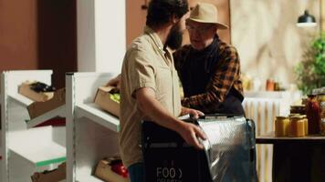 Deliveryman providing organic zero waste supermarket food orders to customers, helped by aged merchant to fill thermic backpack. Man bringing local shop chemicals free groceries to customers video