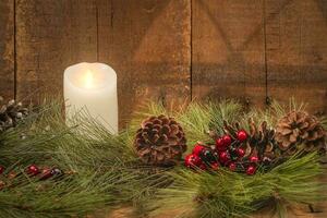 Christmas Candle Glows Bright with Greens Berries and Pinecones on a Wood Background photo