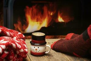 Person Sitting Next to a Fire in Warm Red Socks with Coffee in a Snowman Mug photo