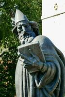 statue of a man holding a book in front of a building photo