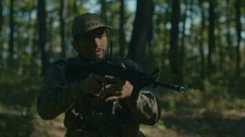 uma mascarado soldado com uma barba anda em cuidadosamente com uma rifle através a floresta video