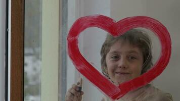 un niño pintura un corazón forma rojo línea en frente de un ventana video