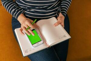 woman makes notes in a notebook while working with a smartphone. green screen photo