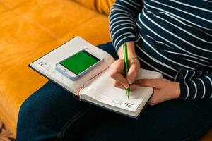 woman, writing notes with a pen in a notebook. using smartphone photo