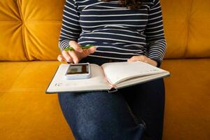 mujer hace notas en un cuaderno mientras trabajando con un teléfono inteligente foto