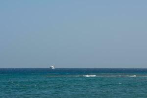 white boat at the horizon of the blue sea with blue sky photo