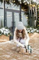 Cute girl in mittens dropped gift boxes on the street in winter near shops photo