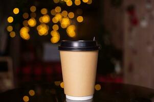 A disposable coffee cup with a lid on the background of a Christmas tree. Place for advertising photo