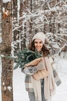 un linda niña con su mano en su sombrero en un Nevado bosque sostiene un paquete con abeto nobilis foto