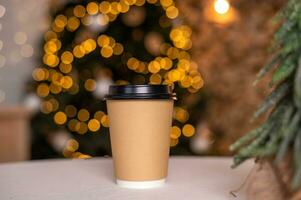 A disposable coffee cup with a lid on the background of a Christmas tree. Place for advertising photo