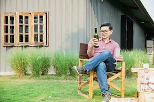 asiático hombre contento pruebas vino para Bebiendo en verde al aire libre jardín foto