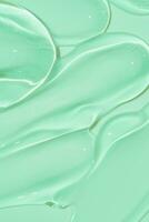textura de crema de frotis cosméticos sobre fondo verde. gota de suero de belleza. muestra de producto transparente y cremoso para el cuidado de la piel. foto