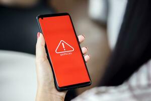 woman using smartphone with warning triangle showing a system error. Concepts of system maintenance, security, anti-virus, and anti-hacking access to critical data. photo