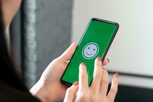 mujer sostiene un teléfono inteligente con contento emoticones en el pantalla a un restaurante. concepto de evaluando cliente satisfacción a muy bueno nivel de cliente Servicio foto