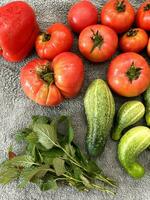 Healthy nutrition Ingredients. Cucumbers and tomatoes, salad greens. Healthy vegetable nutrition. Weight loss program. Heap of whole wet tomatoes and cucumbers on grey terry towel. Top view point photo