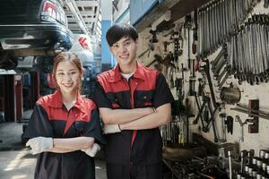 Portrait of two professional Asian mechanic partners smile and arms crossed with hand tools machinery, fixing work at car service garage, maintenance and repair jobs in automotive industry business. photo