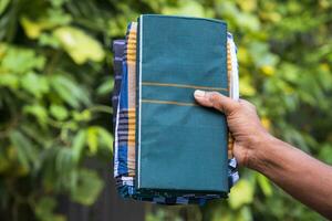 Folded Cotton Fabric Lungi hand holding with Green Blurry Background. Traditional Men's Fashion Lifestyle in Bangladesh photo